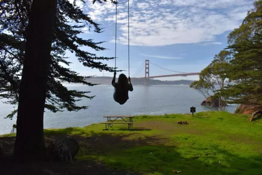 一个女人在金门大桥上空的秋千上摇摆. San Francisco, Californie.